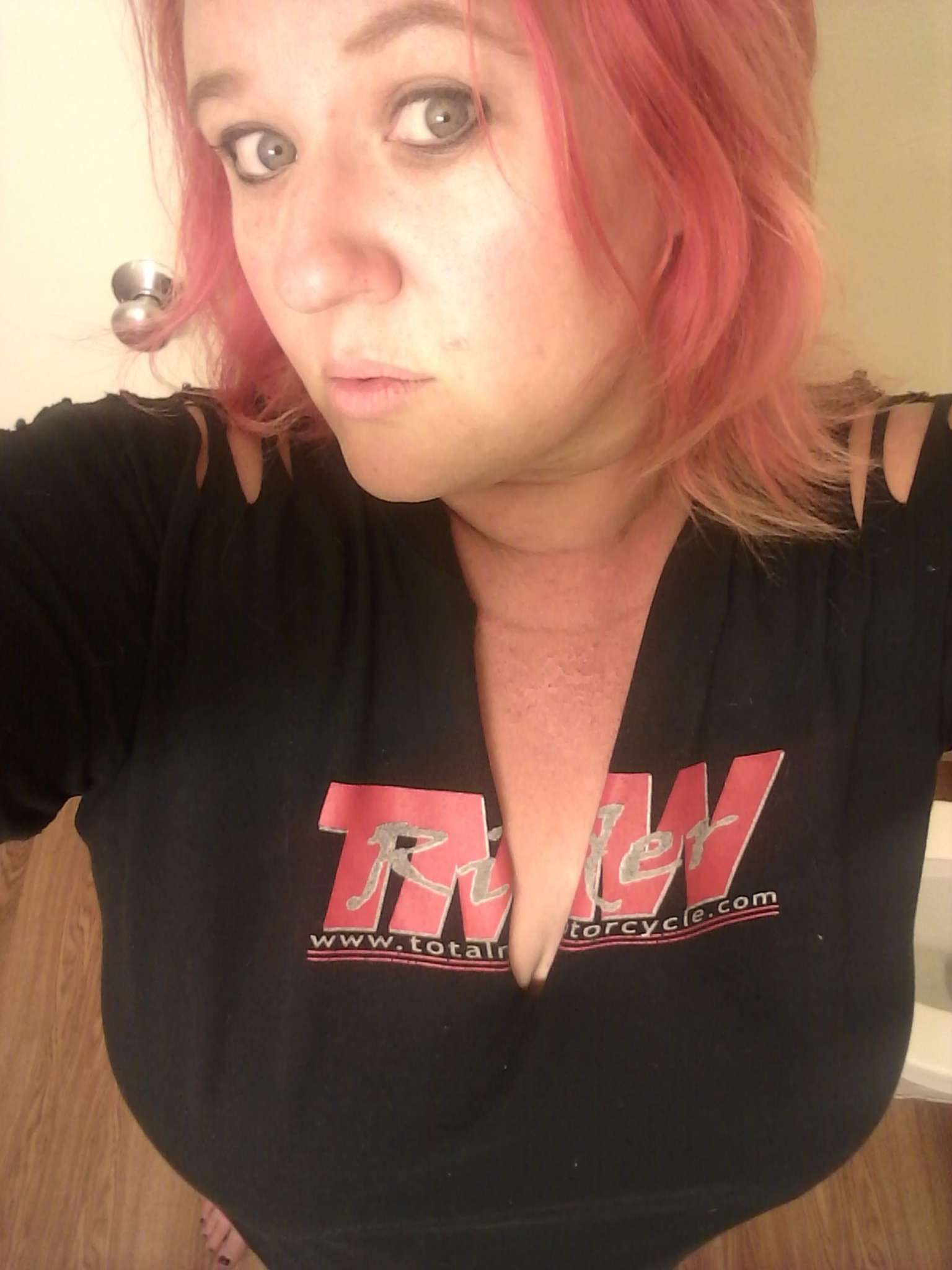 Indian Women's review, A woman with red hair and blue eyes stands barefoot wearing a trendy slashed black t-shirt with the TMW logo. Her makeup is smudged, her hair is mussed and her upper chest appears to be severely sunburned and peeling.