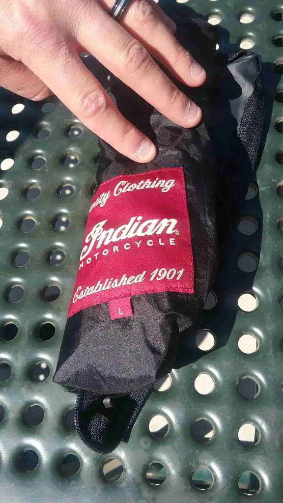 The liner of the Shadow Mesh Jacket is pictured, rolled up tightly to roughly the size of an emergency poncho. A bright red patch bearing the Indian Logo is prominently visible.