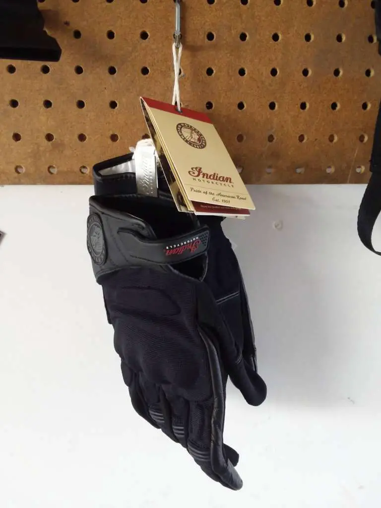 A pair of Passage Gloves hang from a sheet of pegboard, the original label still affixed to the cuffs.