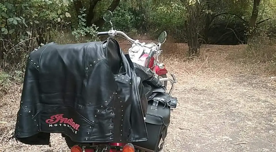 A Shiny red and chrome cruiser motorcycle is parked in a clearing in a forest. It is precisely loaded with black leather luggage.