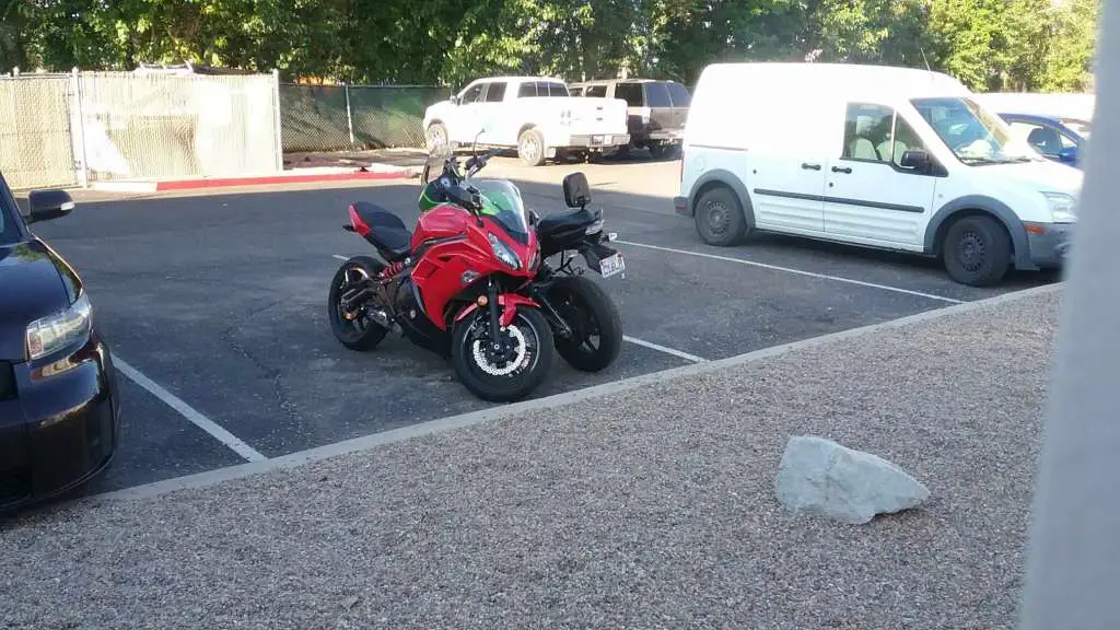 Two Kawasaki sport motorcycles are parked together, facing different directions with the handlebars turned towards each other, taking up minimal space in one parking spot.