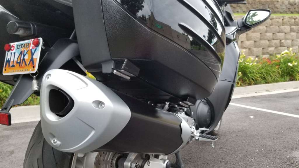 Pictured is the stock exhaust from a low, rearward angle. Prominent is the gray endcap and primarily triangular shape of the silencer.